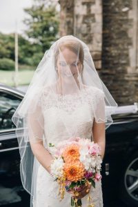a veiled bride holding her bouquet of peach, pink and white flowers.