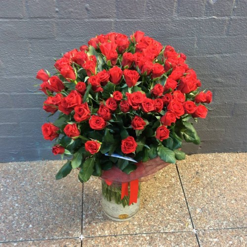 a large cylinder vase filled with 100 long stem red roses.