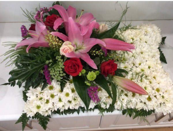 a sympathy pillow tribute of white dasies with a pink oriental lily and red rose feature on the left