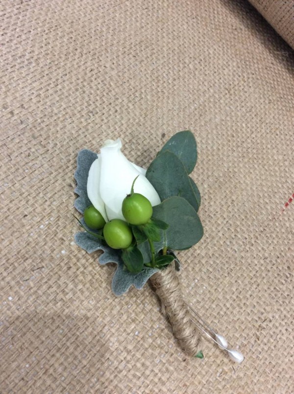 a simple lapel buttonhole with a white rose, green berries and eucalyptus leaves