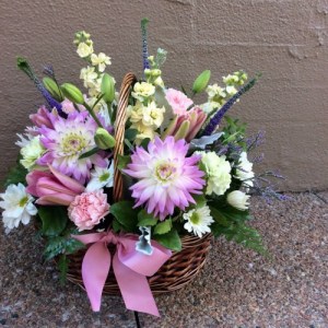 a wicker basket filled with seasonal flowers in pink, white, lemon and lilac