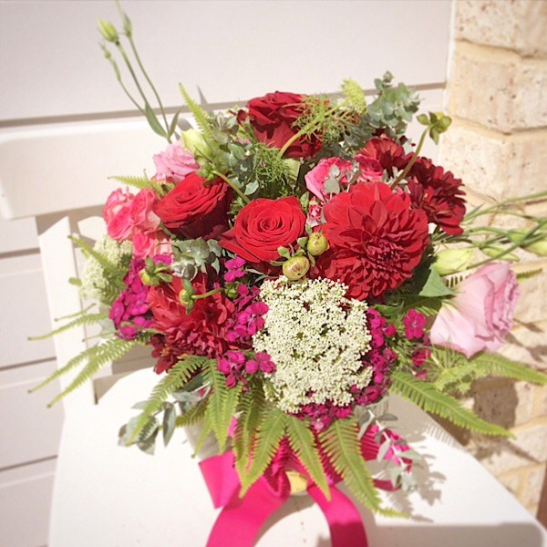 A glass fishbowl arrangement of seasonal red, pink and purple blooms- A Touch of Class Florist