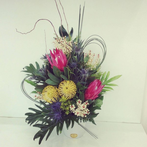 a striking, structural arrangement of native flowers and tropical leaves.