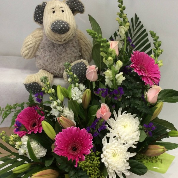 a floral arrangement in pink and purple with a teddy bear