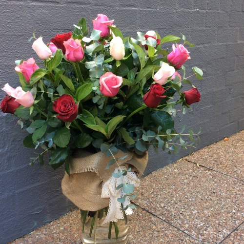 a large glass vase filled with coloured roses and wrapped in hessian with a lace bow.