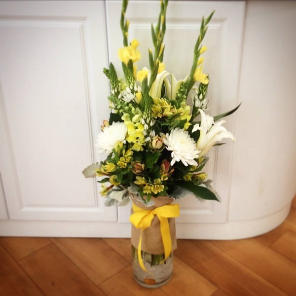 a large glass vase filled with yellow white and green flowers.