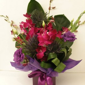 a simple box arrangement of orchids and other seasonal flowers in purple.