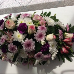a teardrop shaped casket spray of seasonal flowers in pink, purple and white