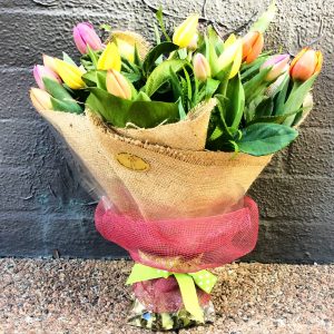 a natural looking hand tied bouquet of mixed coloured tulips. wrapped in hessian and netting.