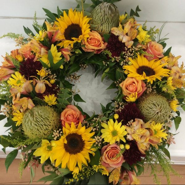 a wreath made using warm coloured fresh flowers. orange, yellow and gold.