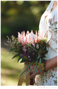 A professional image of a bridesmaid wearing a floral dress carrying a simple wildflower bouquet including a large king protea.