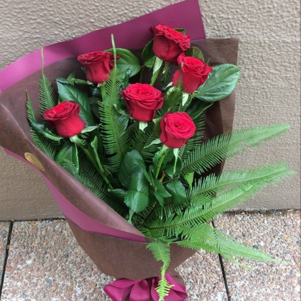 a hand tied bouquet of 6 red roses, wrapped in neutral paper and hessian.- A Touch of Class Florist