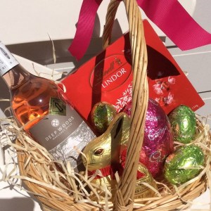 a wicker basket filled with lindt chocolates, a lindt bunny, cadburys eggs and a bottle of rosé wine- A Touch of Class Florist