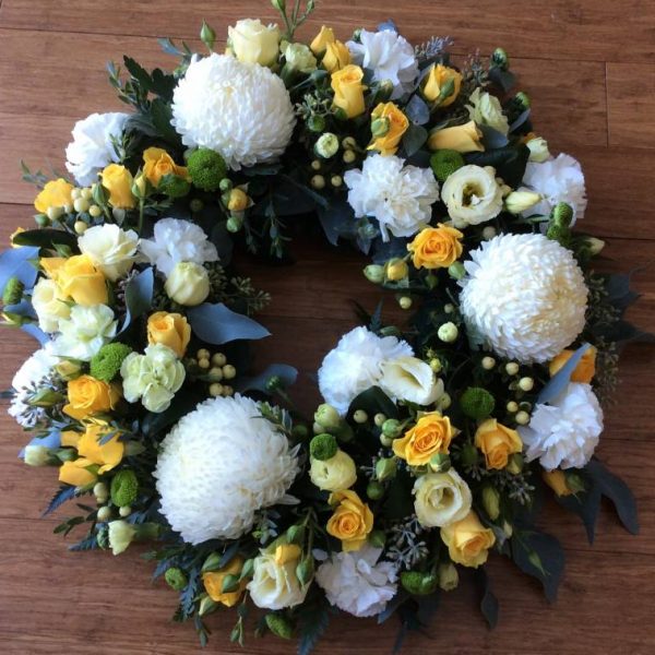 a large floral wreath in soft yellow and white.- A Touch of Class Florist