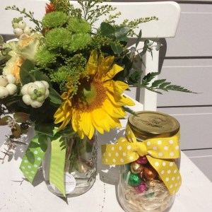a mason jar filled with mini easter eggs and a jar fliled with orange, yellow and green flowers.- A Touch of Class Florist