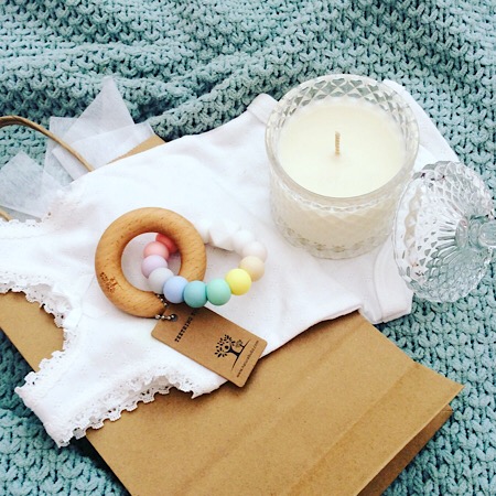 A craft bag of goodies for new parents including Bear and Finn soy scented candle, Nature Bubz teething ring in rainbow and a baby's bodysuit