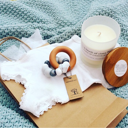 A goodie bag for parents including a Bear and Finn soy, scented candle in with a bamboo lid, a Nature Bubz teething toy in Dove Grey and a baby body suit beautifully packaged in a craft paper bag.
