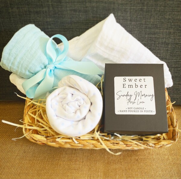 Sweetness Baby Hamper in Blue includes a couple of muslin wraps and an item of baby clothing for bubba and a sweet Ember candle for the parents, gift wrapped in a re-usable basket.