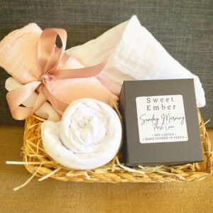 Sweetness Baby Hamper in Pink includes a couple of muslin wraps and an item of baby clothing for bubba and a sweet Ember candle for the parents, gift wrapped in a re-usable basket.