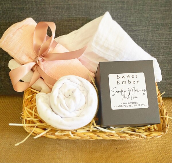 Sweetness Baby Hamper in Pink includes a couple of muslin wraps and an item of baby clothing for bubba and a sweet Ember candle for the parents, gift wrapped in a re-usable basket.